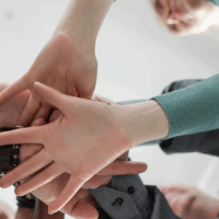 Menschen stehen im Kreis und legen ihre Hände übereinander. Es soll Resilienz in der Gemeinschaft signalisieren.