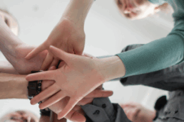 Menschen stehen im Kreis und legen ihre Hände übereinander. Es soll Resilienz in der Gemeinschaft signalisieren.